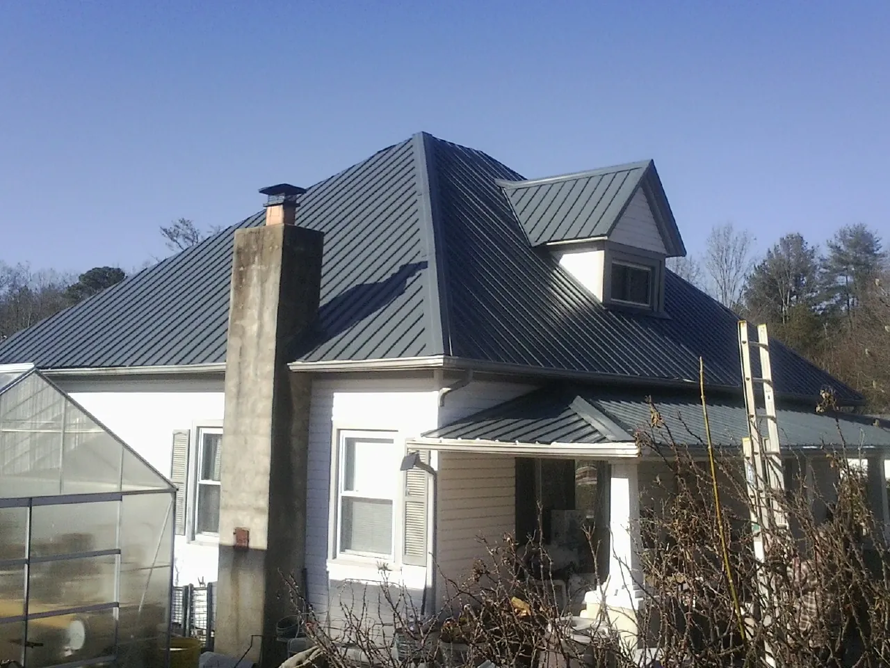 Dark blue standing seam metal roof on a white farmhouse with dormer — Slate & Tile Roof Repair by Roofing Brothers in East Carbon