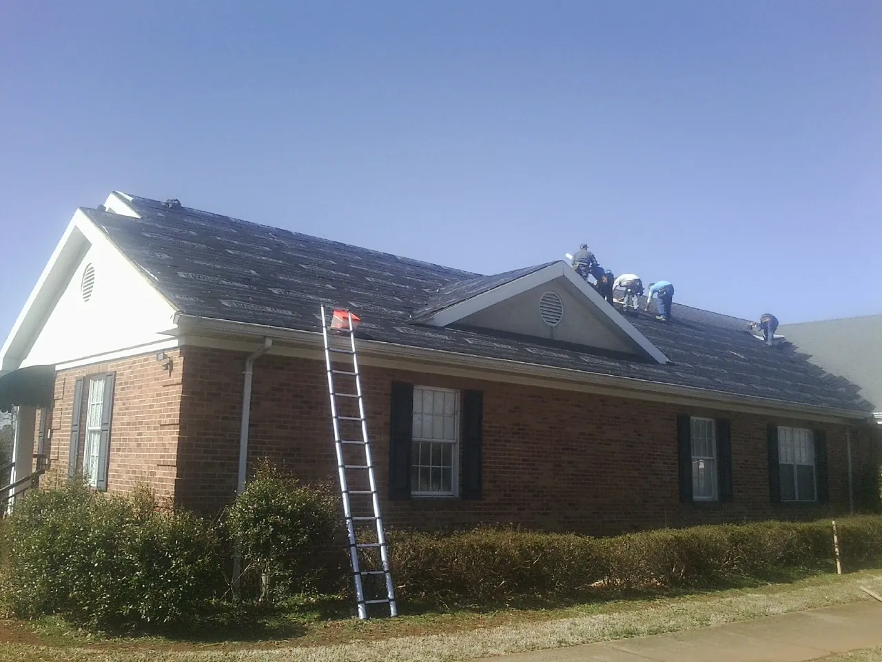 Crew tearing shingles off a brick ranch roof with a ladder set — Metal Roof Repair work by our crew in East Carbon