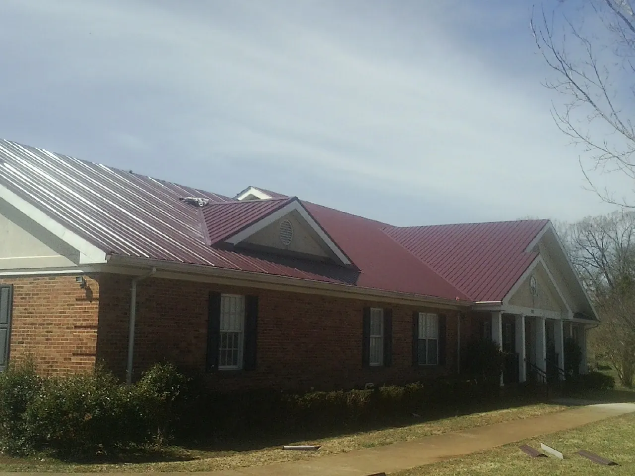 Red metal roof with gabled entries on a long brick building, from a Hail Damage Roof Repair job in East Carbon
