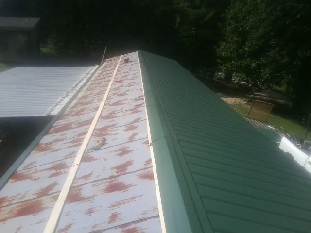Old rusted panels beside newly installed green metal roofing — Wind Damage Roof Repair by Roofing Brothers in East Carbon