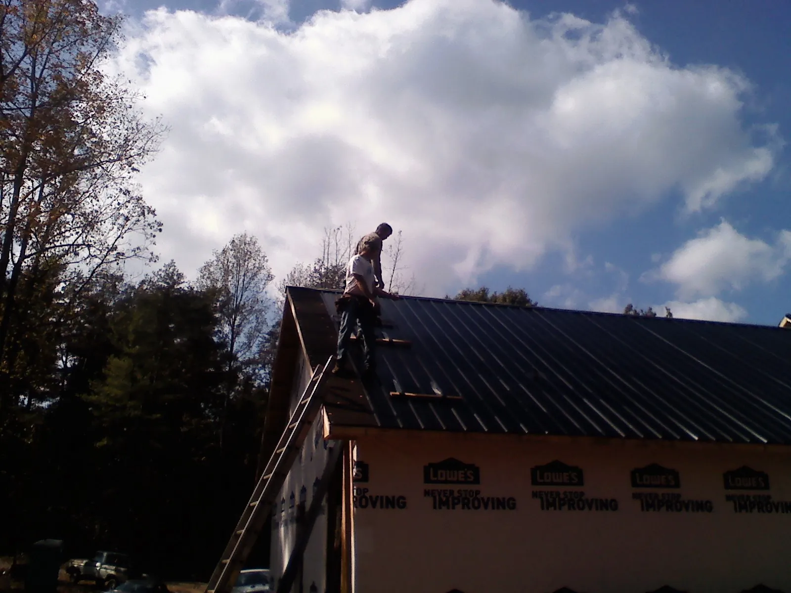 Roofer fastening dark metal panels high against a cloudy sky, from a Roof Inspection job in East Carbon