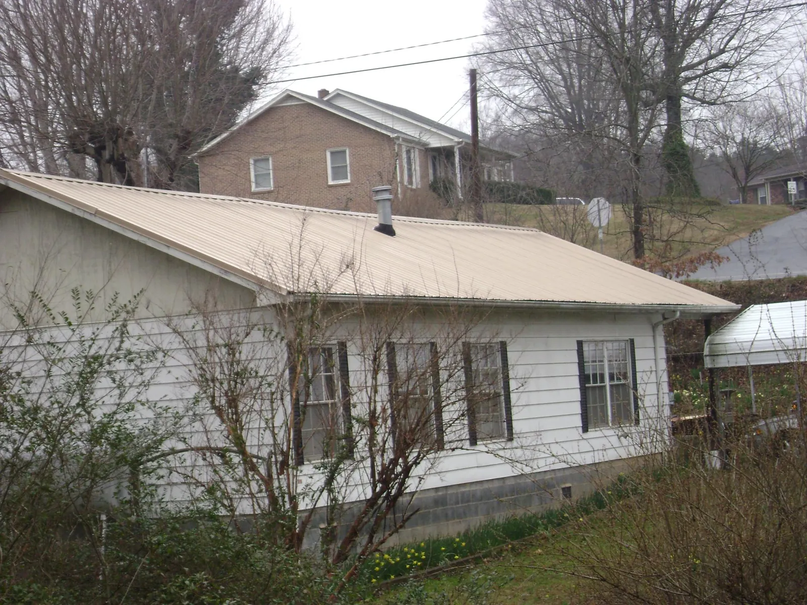 Tan metal roof on a white sided house set into a hillside — Commercial Roofing by Roofing Brothers in East Carbon